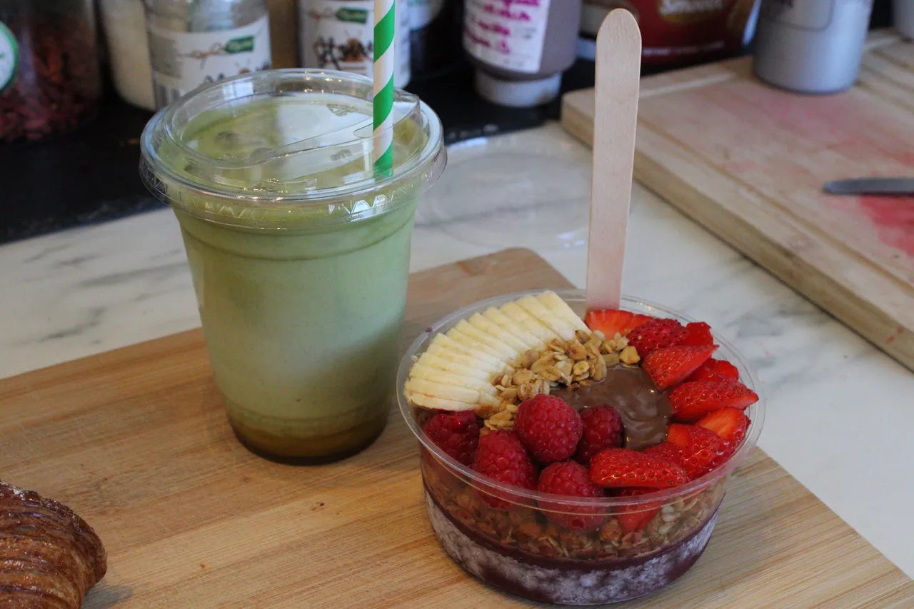 An açaí bowl topped with fruit and granola, beside a matcha smoothie